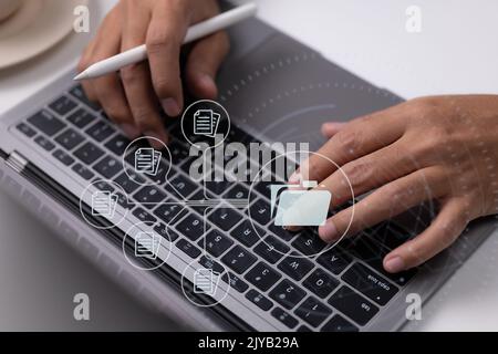 Paperless workplace idea based on e-documents. On a virtual screen, a businessman works on a laptop computer keyboard with electronic document icons. Stock Photo