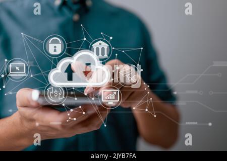 A guy uses a smartphone while holding a cloud computing diagram. Cloud computing, data storage, networking, and internet service principles. Stock Photo