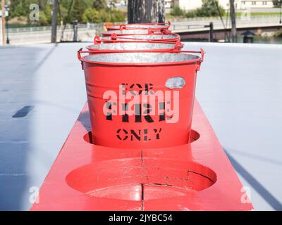 Row of red buckets in rack with sign for fire only for emergency. Stock Photo