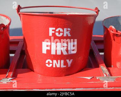 Bright red buckets labeled in white For Fire Only ready as protection in case of fire., Stock Photo