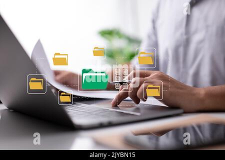 Paperless office idea based on electronic documents. A businessman types on a laptop keyboard while looking at icons for digital documents on a comput Stock Photo