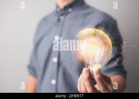 Businessman hand holds a lit light bulb with a network connecting line, representing the concepts of idea, innovation, and inspiration. Lights glow an Stock Photo