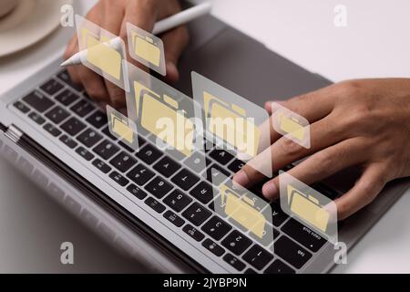 Paperless workplace idea based on e-documents. On a virtual screen, a businessman works on a laptop computer keyboard with electronic document icons. Stock Photo