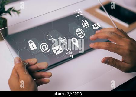 In a modern workplace with virtual icons interface, a businessman works with a digital tablet, a book, and a document. Stock Photo