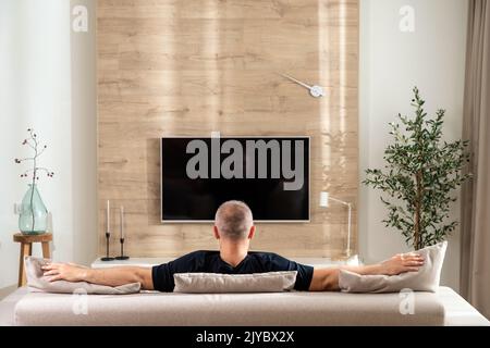 Man in a relaxed position on the sofa in the living room in front of the TV Stock Photo