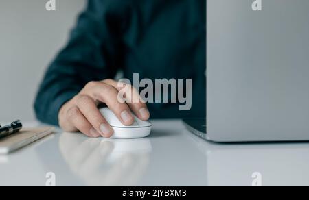 A man hand holds a computer mouse and types on a laptop keyboard. Stock Photo