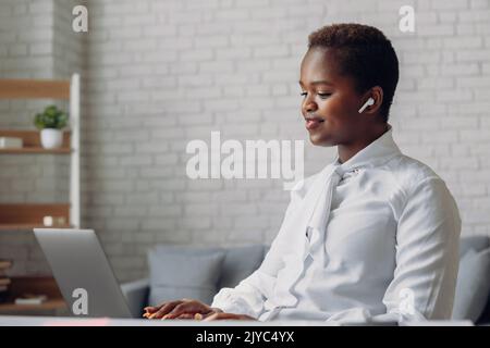 Happy young Afro American entrepreneur woman sitting working on laptop in office. Achievement career concept. Co-working space with opened laptop Stock Photo
