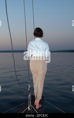 Beautiful woman in casual clothing standing on the bow of a sailing yacht Stock Photo