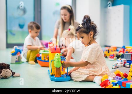 Nursery school. Toddlers and their teacher playing with colorful plastic playhouses, cars and boats. Imagination, creativity, fine motor and gross motor skills development. High quality photo Stock Photo