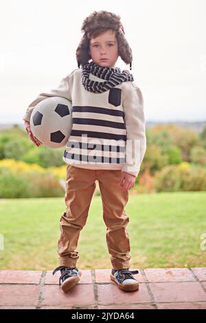 I wish I had a friend to play with. a little boy standing outside in rainy weather with his soccer ball. Stock Photo