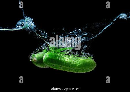 Two fresh cucumbers dropped underwater with splashes isolated on black background. Stock Photo
