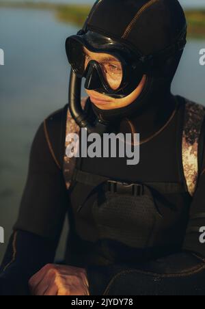 Young scuba diver looking away while wearing a scuba gear and a wetsuit. Adventurous young man going scuba diving by the sea. Stock Photo