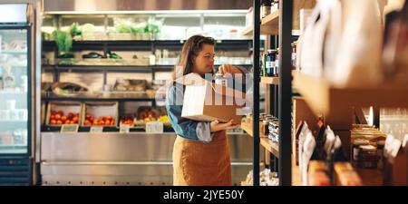 Shop employee with Down syndrome restocking food products in a grocery store. Empowered woman with an intellectual disability working as a shopkeeper Stock Photo