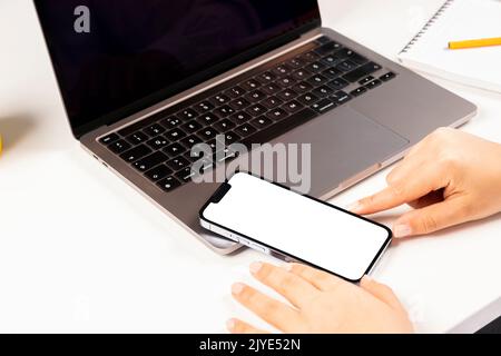 Modern smartphone mock up, selective focus on woman hands holding modern smartphone mock up.  Office desktop set up with laptop and mobile phone. Stock Photo