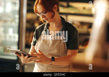 Cheerful supermarket owner using a digital tablet while standing in her grocery store. Successful entrepreneur running her small business using wirele Stock Photo