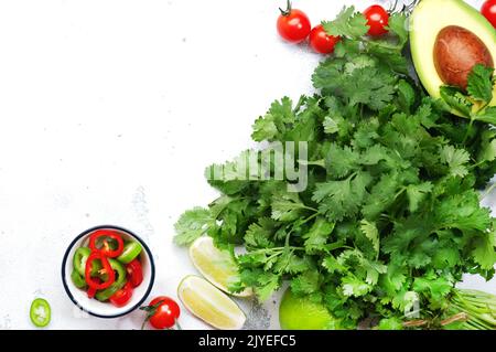 Fresh cilantro or coriander, chili and jalapeno peppers, avocado, lime and cherry tomatoes - ingredients for Mexican spicy cuisine. White kitchen tabl Stock Photo