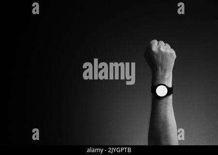 Black and white image of man's hand with smart watch on wrist, displaying blank white screen, isolated on dark background with copy space Stock Photo