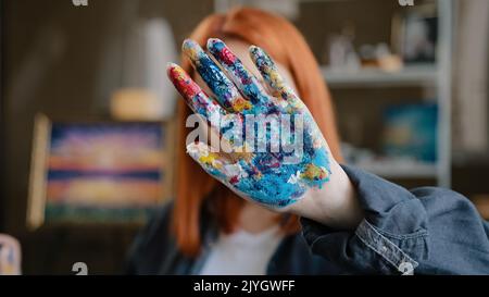 Female calm red-haired girl artist lady Caucasian 30s woman painter designer holding hand in front stop gesture not no gesture showing dirty in Stock Photo
