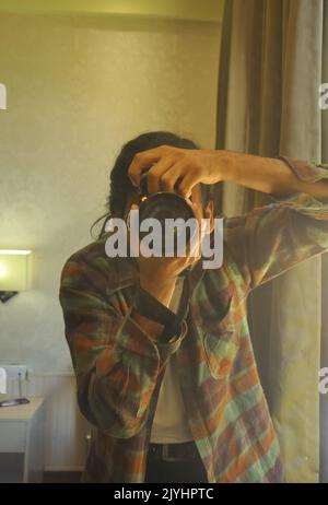 A male photographer taking selfie with his DSLR camera in front of mirror inside the bedroom. Stock Photo