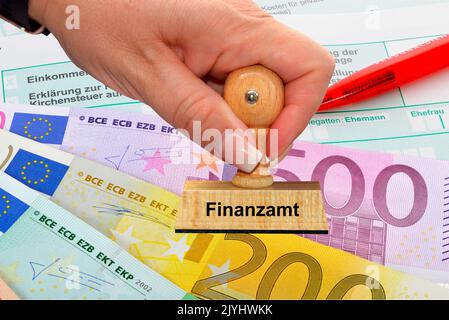woman's hand with stamp lettering, Finanzamt, taxation office, Euro bills an pencil in the backgound, Germany Stock Photo