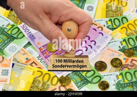 woman's hand with stamp lettering 100 billions Sondervermoegen, 100 special asset, Euros in the background, Germany Stock Photo