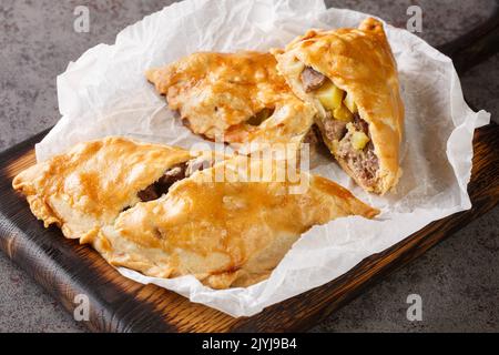 Cornish Pasty Baked pie filled with meat and potatoes closeup on the paper on the wooden board. Horizontal Stock Photo