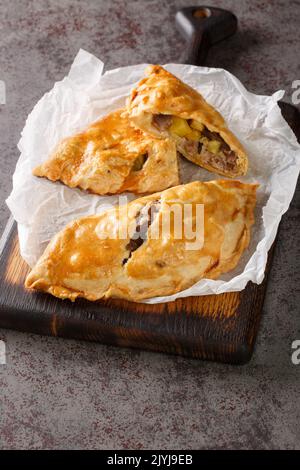 Traditional Cornish pasty filled with meat potato swede and carrot closeup on the paper on the wooden board. Vertical Stock Photo