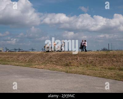 Doel, Belgium, 21 August 2022, People walk on the embankment of the river Scheldt with a dramatic cloud field and industry in the background Stock Photo