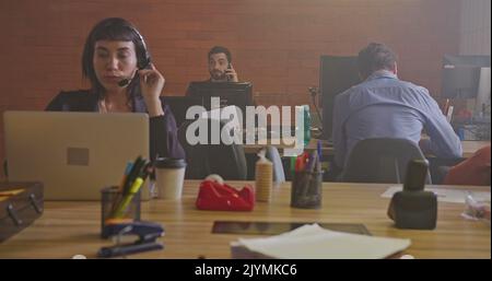 Group of people working inside corporate office at night. Young men and women employees in front of computers. Workspace and businesspeople concept. M Stock Photo