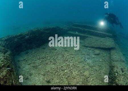 Scuba diver goes up the steps leading to the entrance to a small swimming pool in the thermal complex of Lacus Baianus, Marine Protected Area of Baia, Naples, Italy, Tyrrhenian Sea Stock Photo