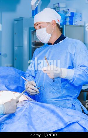A young doctor performs surgical treatment of a patient in the operating room. Stock Photo