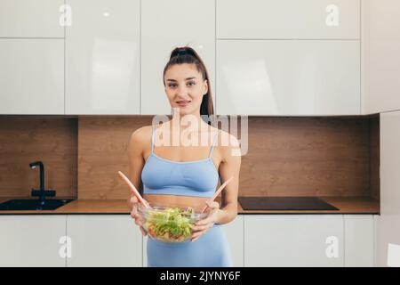 Young beautiful female nutritionist showing ready fresh vegetable salad, looking at camera, smiling Stock Photo