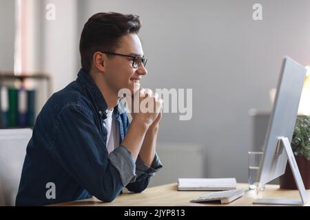 Young Male Entrepreneur Looking At Computer Screen In Office And Smiling Stock Photo