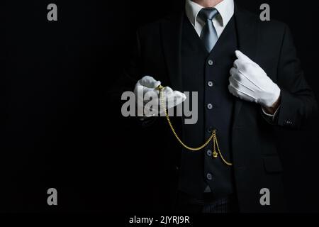 Portrait of Butler in Dark Suit and White Gloves Holding Gold Pocket Watch. Vintage Style and Professional Courtesy. Stock Photo
