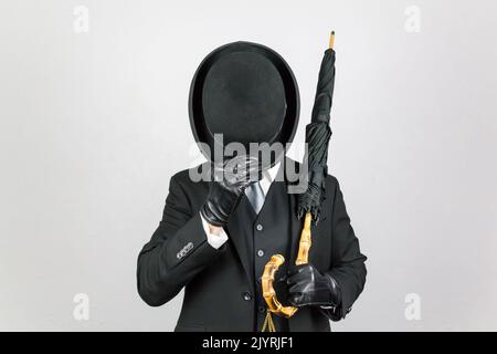 Portrait if English Gentleman in Dark Suit Doffing Bowler Hat and Holding Umbrella. Classic British Butler. Stock Photo