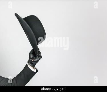 Isolated Image of Gentleman in Dark Suit and Leather Gloves Politely Doffing Bowler Hat. Classic British Butler or British Businessman. Stock Photo