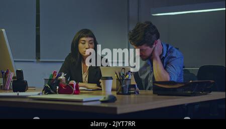 Focused two employees sitting at office late at night feeling pressure under deadline. people being overworked seated at desk feeling frustration. Mal Stock Photo