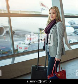 Shes leaving on a jet plane. Portrait of a young woman standing with her luggage in an airport. Stock Photo