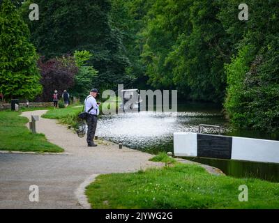 Relaxing recreational activities for people by scenic Leeds and Liverpool Canal (walkers, person angling) - Gargrave, North Yorkshire, England, UK. Stock Photo