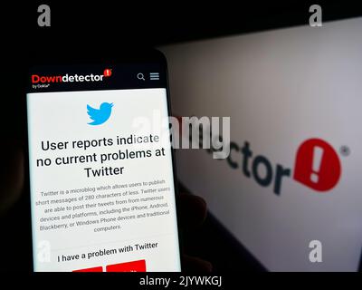 Person holding smartphone with website of platform Downdetector and Twitter status in front of logo. Focus on phone display. Stock Photo