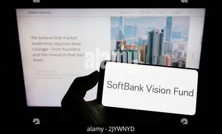 Person holding smartphone with logo of venture capital fund SoftBank Vision Fund on screen in front of website. Focus on phone display. Stock Photo