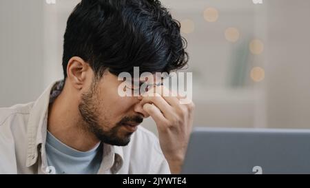 Close-up male focused arabic young guy business man freelancer looking at laptop tired discomfort in eyes pain worrying problem bad news takes off Stock Photo