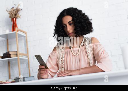 KYIV, UKRAINE - JUNE 29, 2022: thoughtful fortune teller looking at tarot card at home Stock Photo