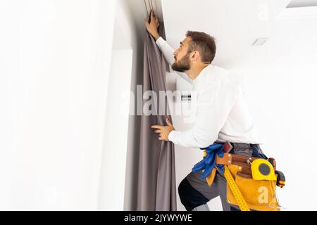 Young man installing curtains over window. Stock Photo