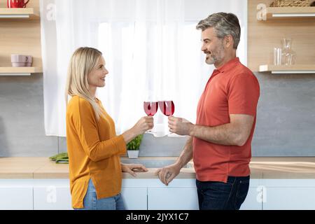 Romantic middle aged couple drinking red wine at kitchen Stock Photo