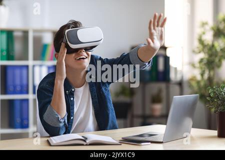 Young Man Wearing VR Glasses Touching Virtual Screen While Sitting At Workplace Stock Photo