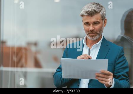 Smiling mature businessman standing outside of office with documents Stock Photo
