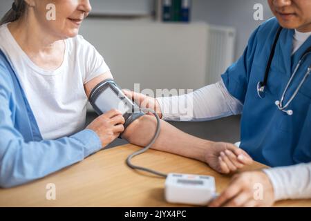 Concentrated adult asian male doctor measures pressure with tonometer to old woman patient in clinic Stock Photo