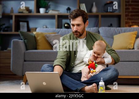 A young father, with a child, does housework. Father on maternity leave. Dad cheerfully sings, dances and vacuums, cleans with a small child in his Stock Photo