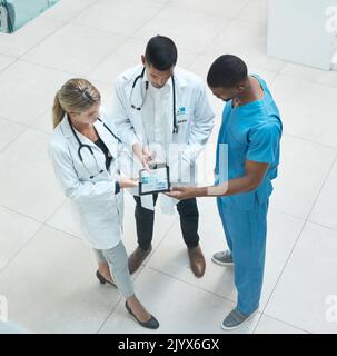 Group of doctors working on digital tablet while standing in the hospital hallway and talking. Top view of healthcare employees analyzing test results Stock Photo